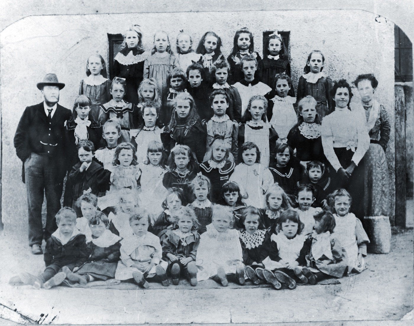 Tynehead School. Teacher at right Sophia Dent (1881-1931), the male teacher said to be Johnny Dent (!894-1919). If the photograph had been taken before 1894 then the man could have been Robert Dent,  (1847-94). If it was Tynehead then Sophia might have shared in responsibilties? The 2 windows + larger one look the same as Tynehead school.
At the turn of the century Sophia would have been 19 years old. Some of the fashions wouldn't have been out of place in the 1890s but could as easily be from the first decade of the C20. The standard of dressing and plump, well-fed faces might imply relatively good times economically.
All the older pupils are girls. Where were the boys at this time?